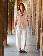 Load image into Gallery viewer, A woman stands in a stone corridor wearing a light blush pink button-up shirt, off-white wide-leg cropped pants, and dark brown loafers.