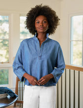 Load image into Gallery viewer, Woman wearing a blue shirt standing in a room with large windows.