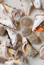 Load image into Gallery viewer, Decorative earrings with shell-like designs and gemstone embellishments on a textured surface.