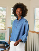Load image into Gallery viewer, Woman wearing a blue shirt standing in a room with large windows.