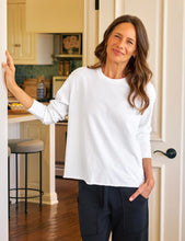 Load image into Gallery viewer, Woman in a white sweater and dark pants standing in a kitchen.